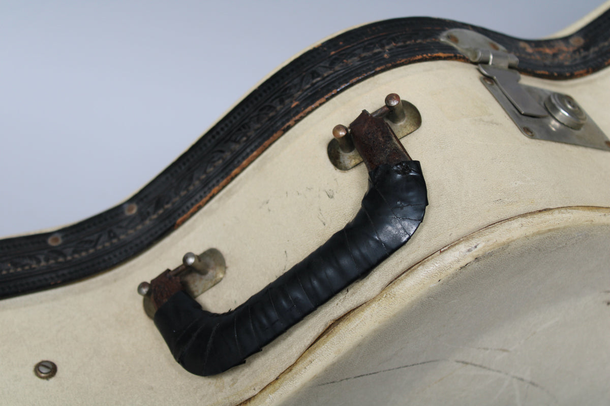 Close-up of the tan case's handle, wrapped in black tape, with a corroded latch and decorative black trim along the edge.