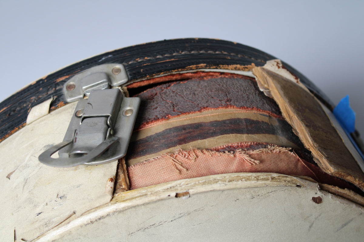 Close-up of a tarnished metal latch on the tan case, revealing worn black binding and frayed interior lining.