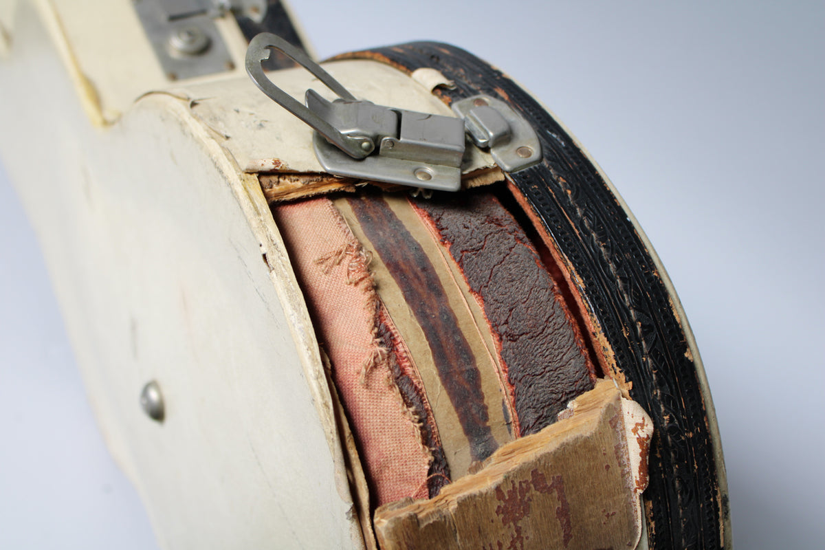A close-up of the tan case shows a silver latch, with the case's worn, exposed layers of wood, fabric, and black trim.