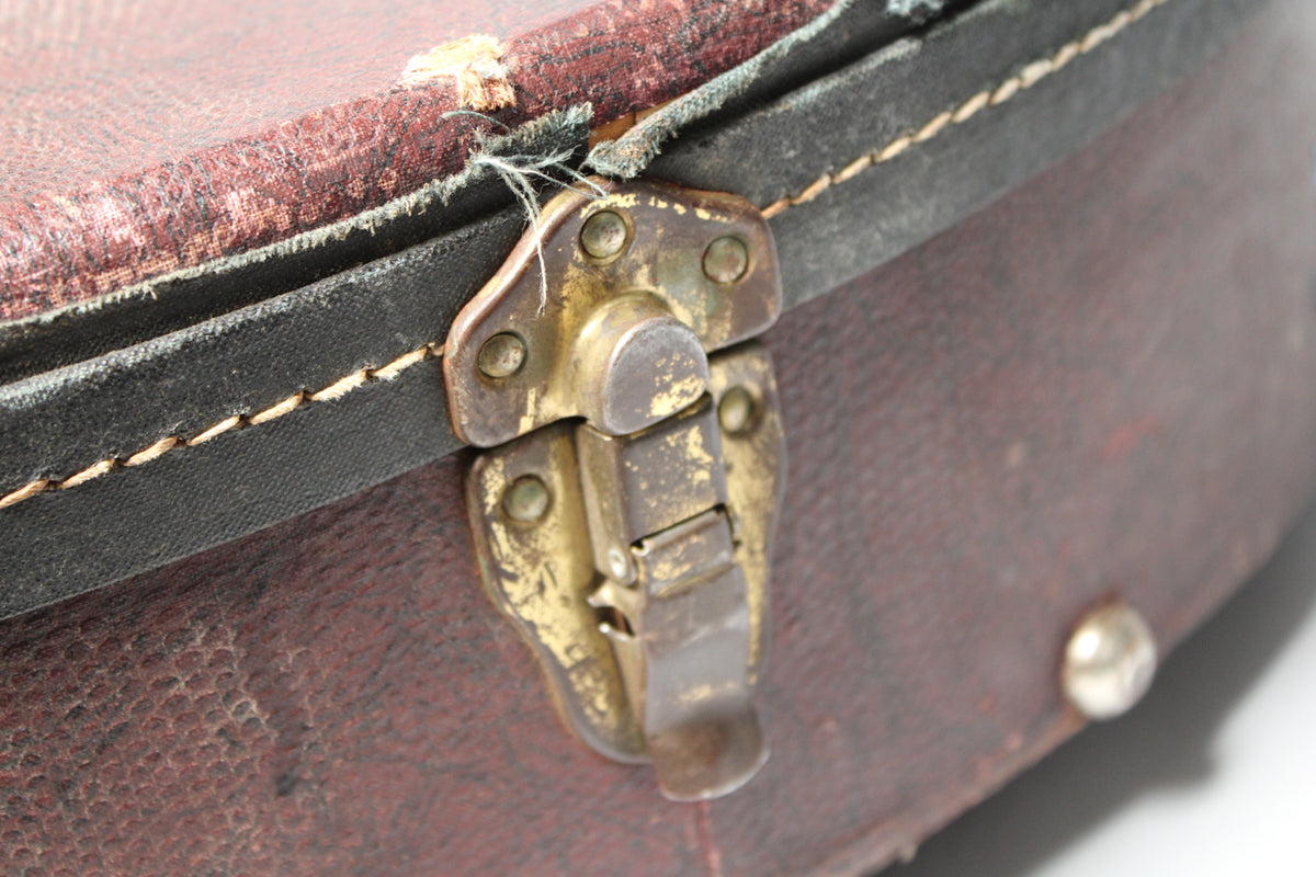 Close-up of a tarnished brass latch on the brown snakeskin case, with worn edges and exposed fabric near the hinge.