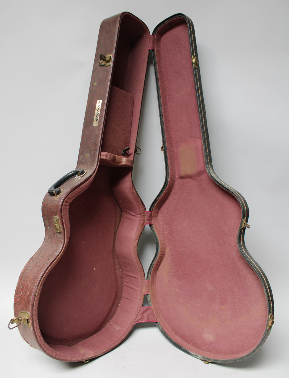 Open brown snakeskin-patterned guitar case with a black handle, brass latches, and worn, dusty maroon velvet lining.