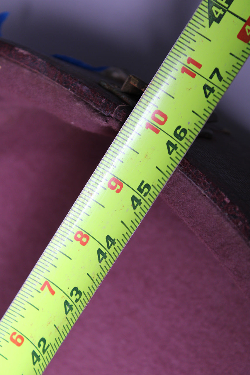 A bright yellow measuring tape diagonally crosses the image, showing inches and centimeters over the case's dark brown exterior and purple interior.
