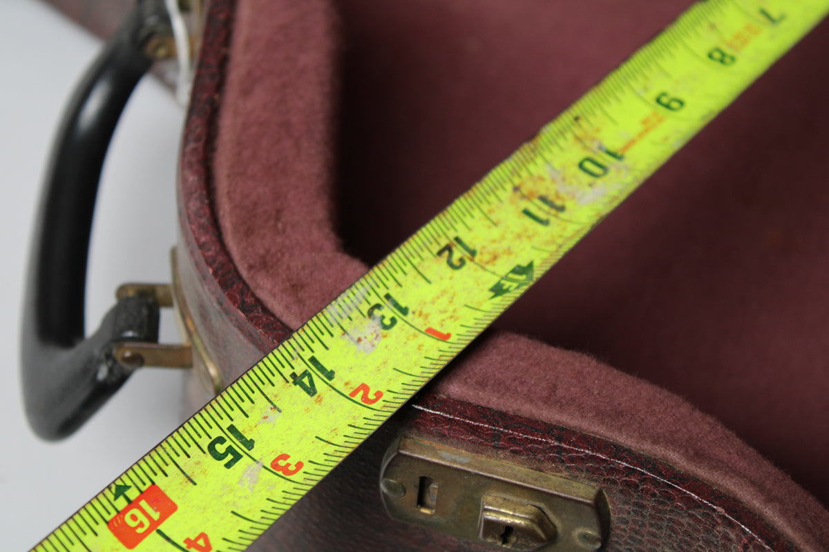 A yellow tape measure spans the open brown snakeskin case, revealing a burgundy plush interior and a brass latch.