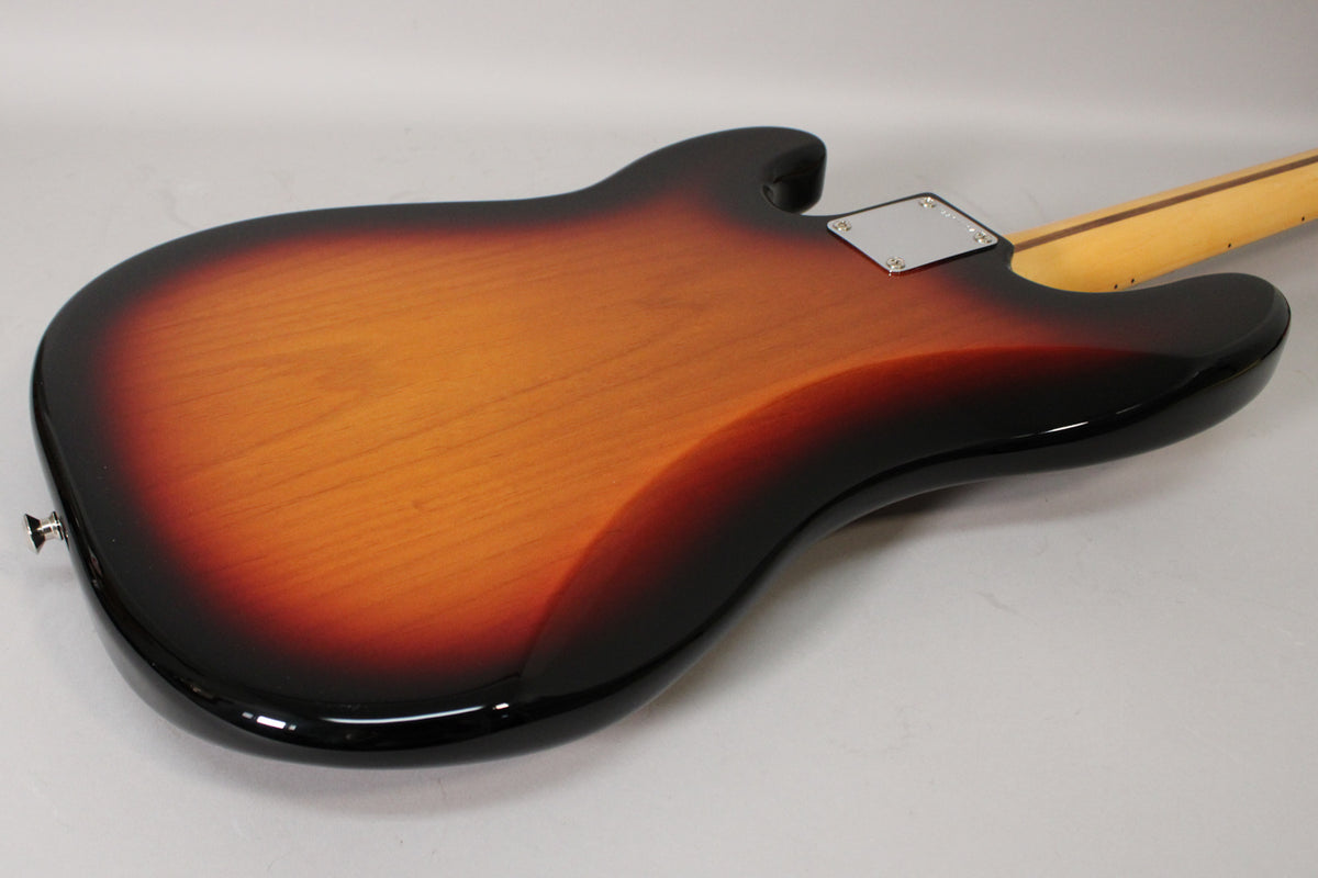 The bass's sunburst body is viewed from the back, showing a chrome neck plate and a strap button on the lower horn.