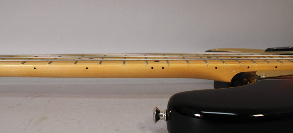 Side view of the sunburst bass body and neck, showing the maple fretboard with black dot inlays and a chrome strap button.