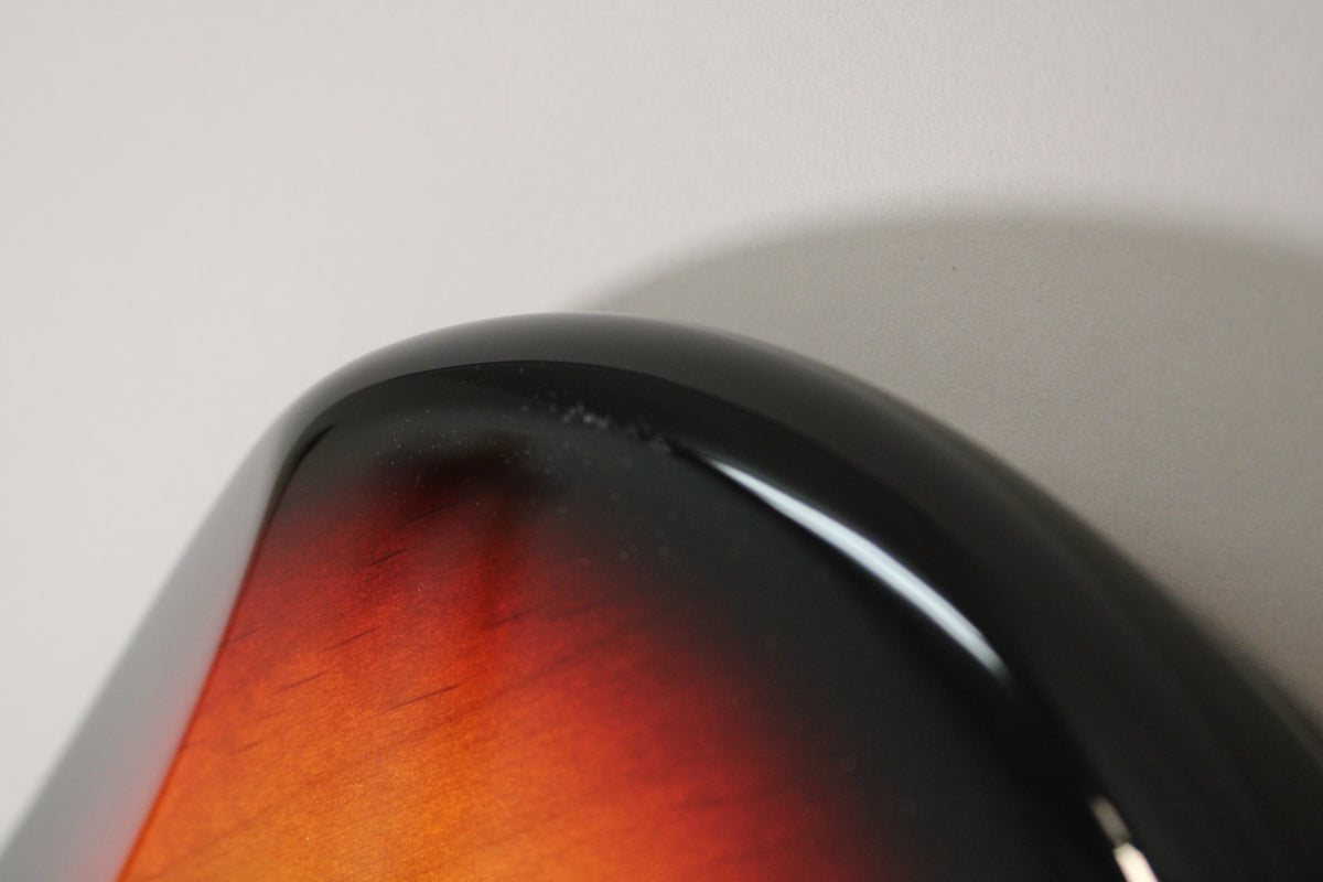 Close-up of the sunburst body's upper curve, showing finish checking and small chips along the black edge.