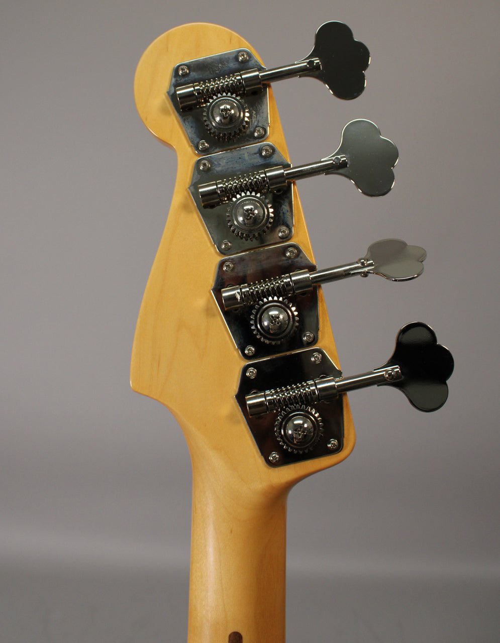 Rear view of the bass headstock and upper neck, showing four chrome clover-leaf tuners on a light wood finish.