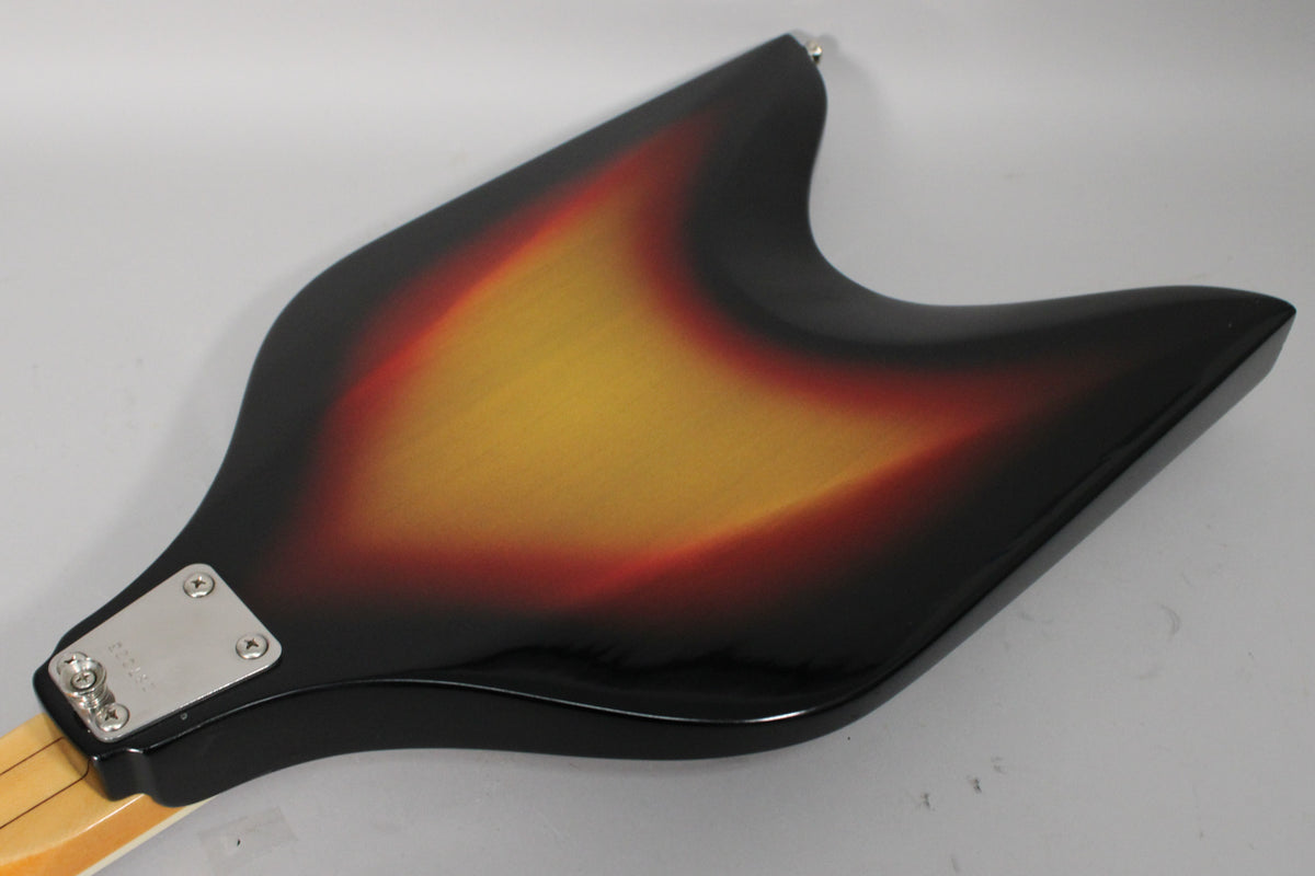 The back of a V-shaped sunburst bass, angled from the neck joint to the upper bout, showing a chrome neck plate.