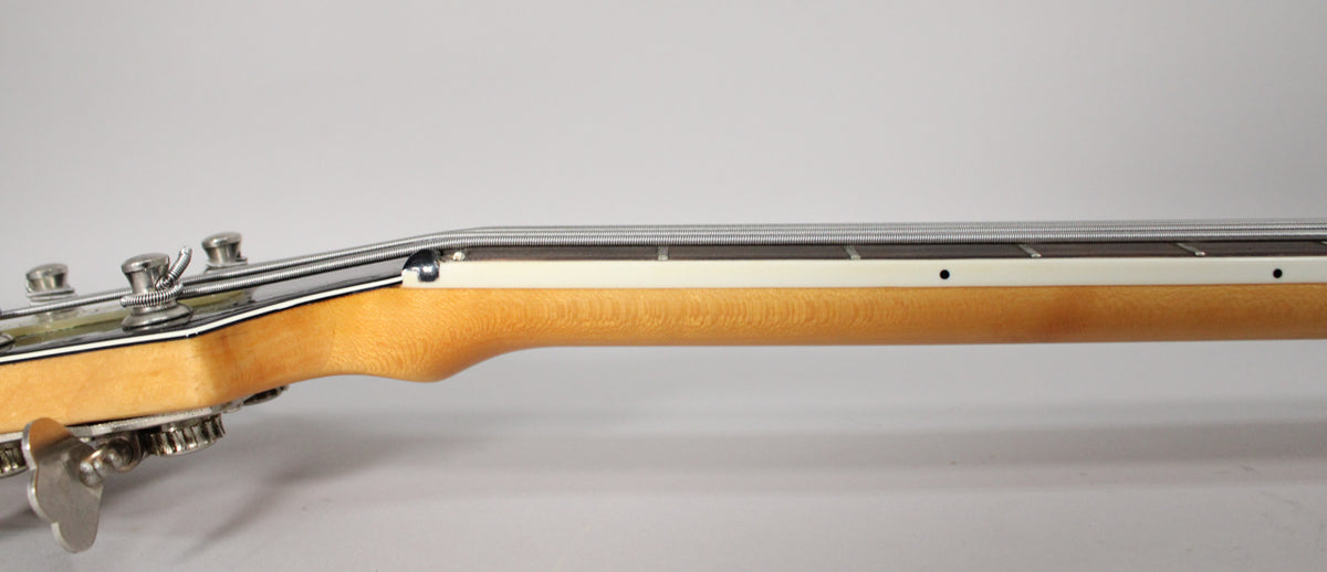 Side view of the bass neck, showing the light wood grain, white binding, dark fretboard, and chrome tuning pegs.
