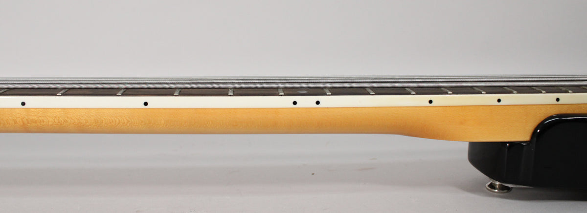 The bass neck, with a light wood finish and dark fretboard, is shown from the side, revealing white binding and black dot inlays.