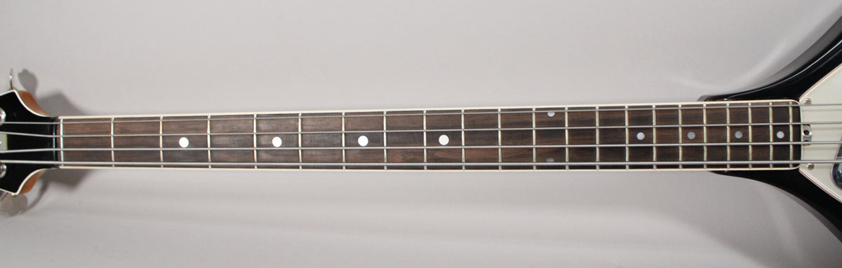 The bass guitar's dark fretboard with white dot inlays and frets is centered, showing the headstock and part of the black body.