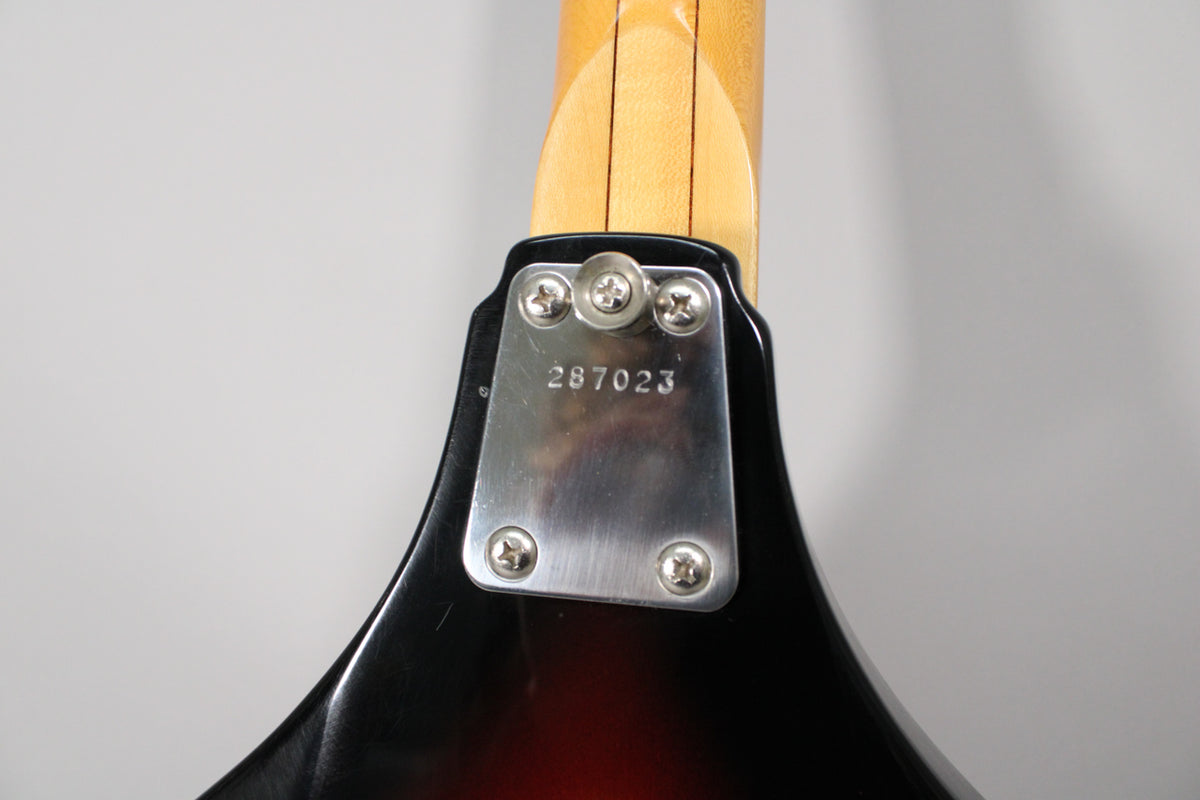 Close-up of the bass's neck heel, showing the 4-bolt neck plate with serial number 287023 and light wear on the sunburst finish.