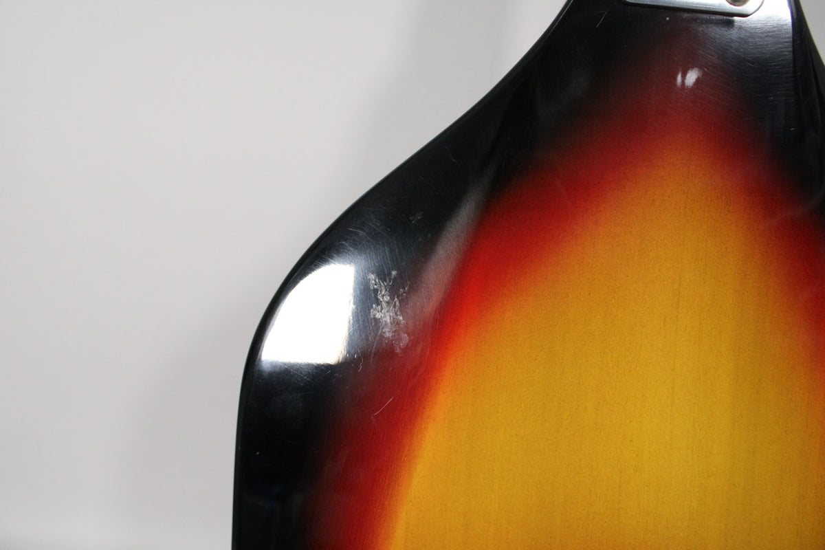Close-up of the bass's upper body, showing the sunburst finish with black, red, and yellow, and notable finish wear on the black edge.