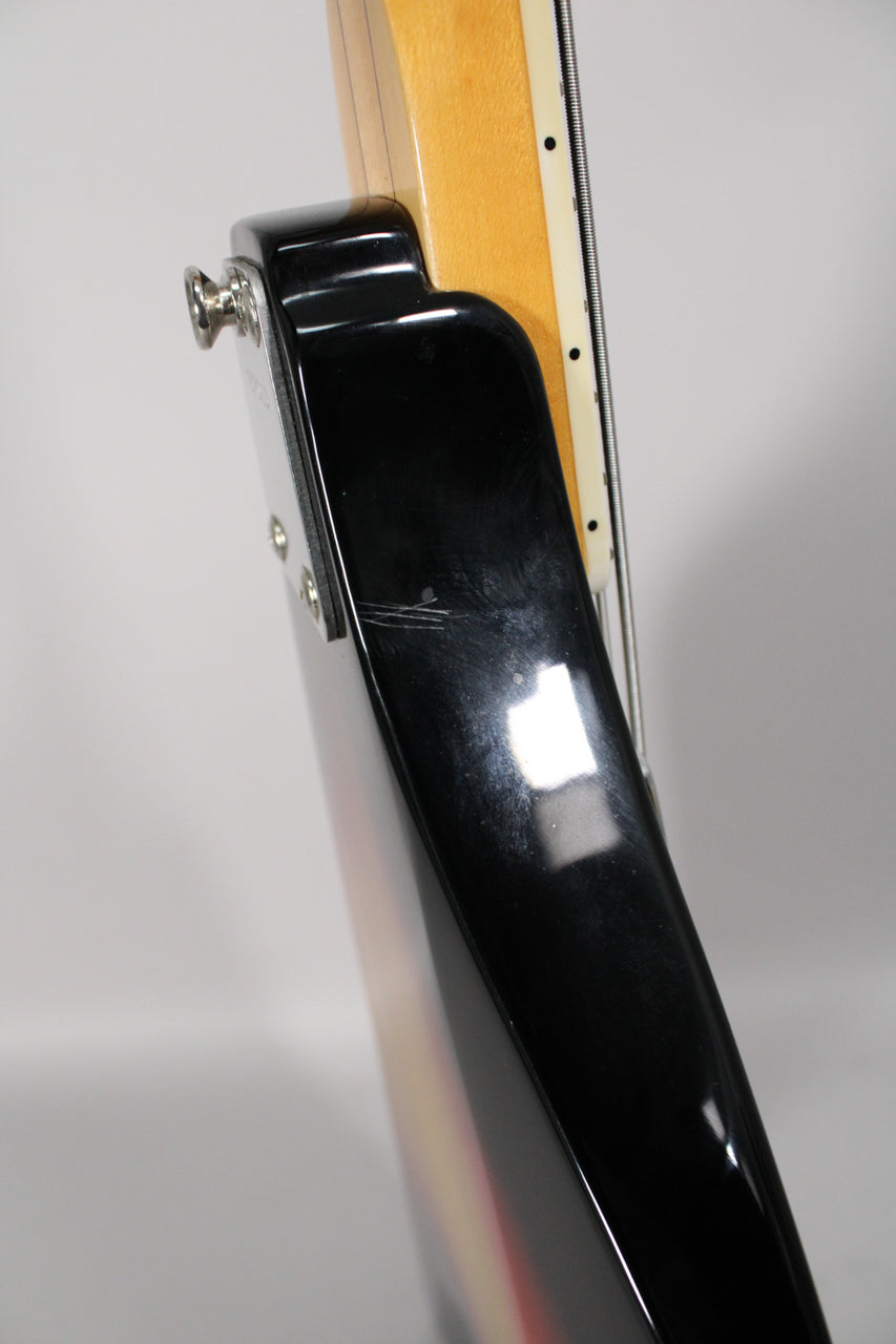 Close-up of the bass's upper horn, showing the sunburst finish, neck plate, strap button, and light scratches on the black finish.