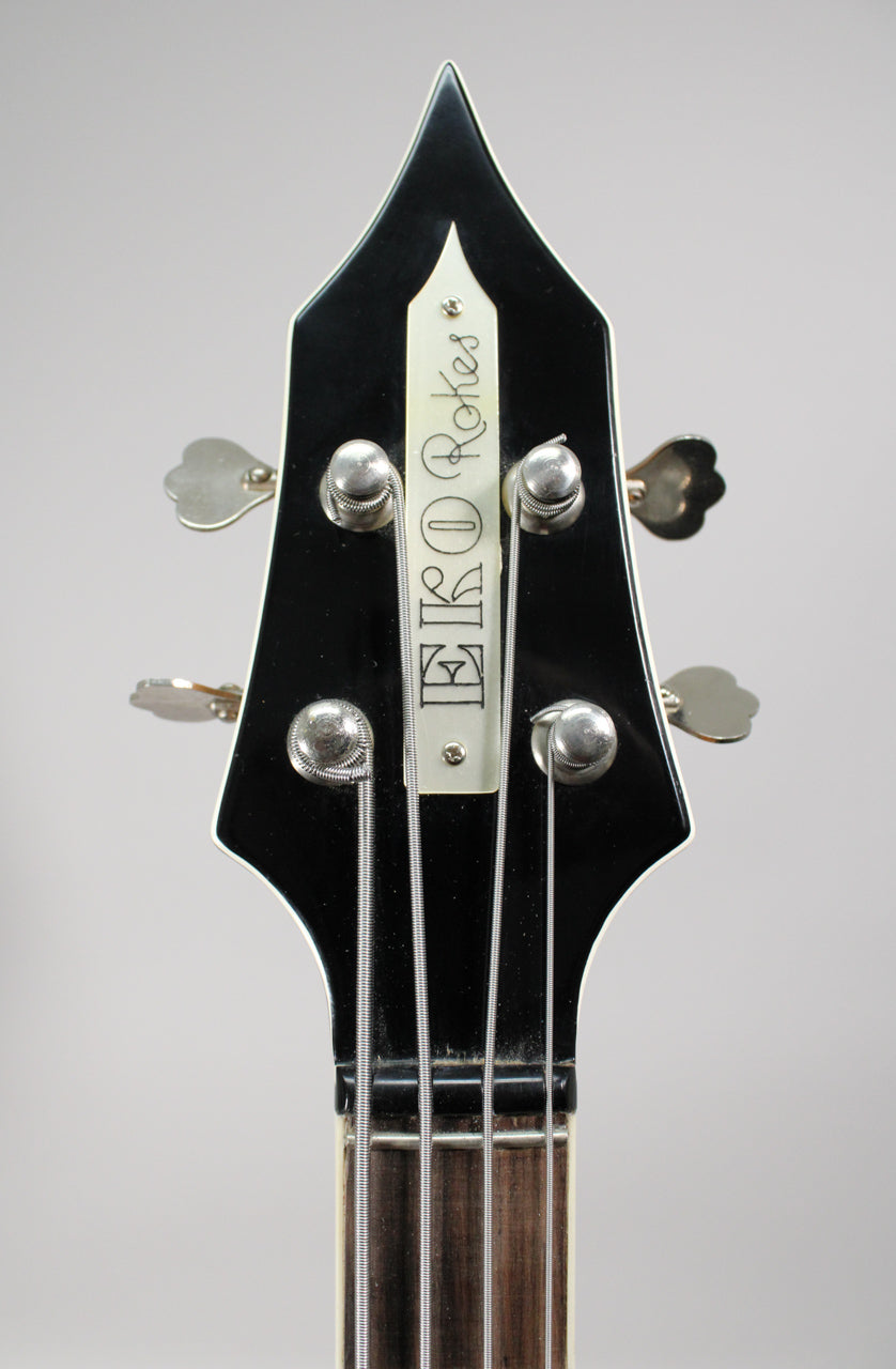 The black, pointed headstock with white binding and four clover-leaf tuners shows some dust and minor wear around the nut.