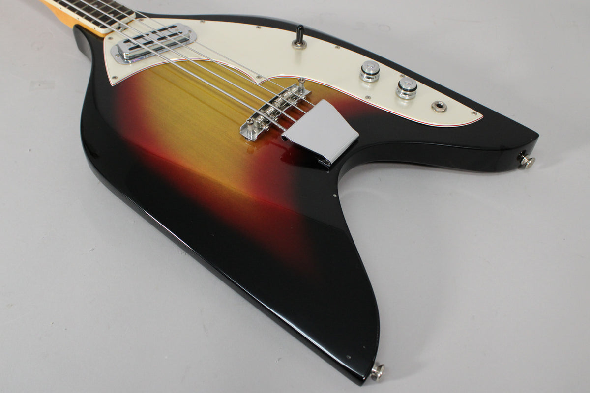 The bass body, angled from above, shows a sunburst finish, white pickguard, chrome pickup, bridge, and three control knobs.