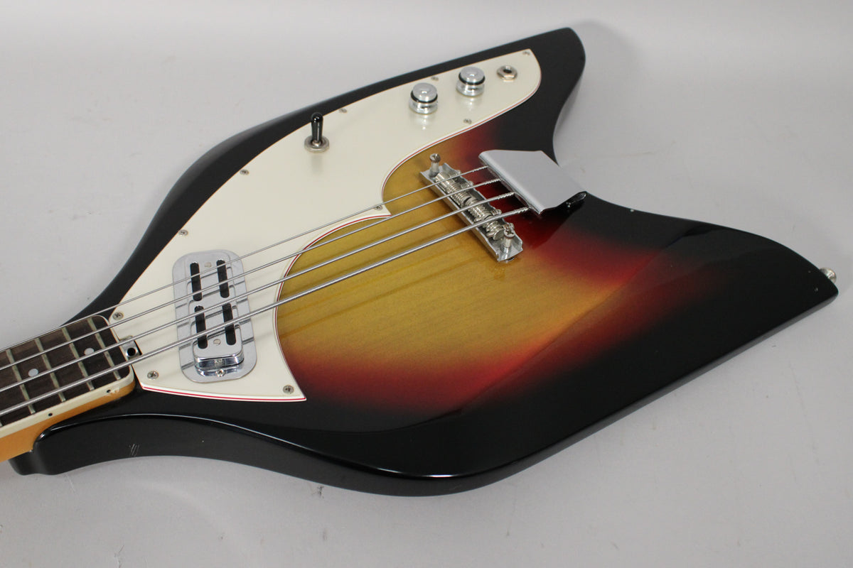 The bass body, with a sunburst finish and cream pickguard, shows a chrome bridge cover and three control knobs.