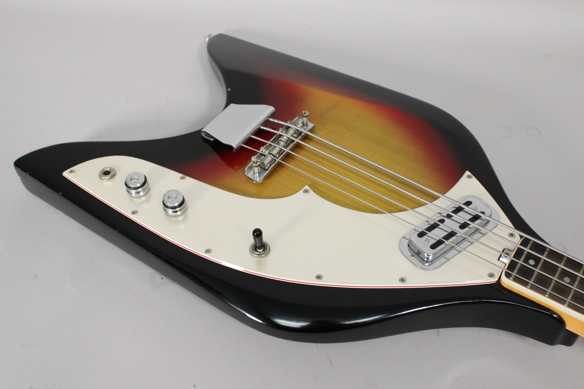 Close-up of the bass body, showing the sunburst finish, white pickguard, chrome bridge, single pickup, and three control knobs.