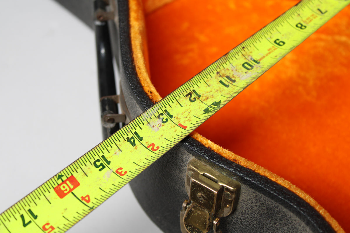A yellow tape measure spans the open black case, showing 16 inches across the orange plush interior, with a brass latch visible.