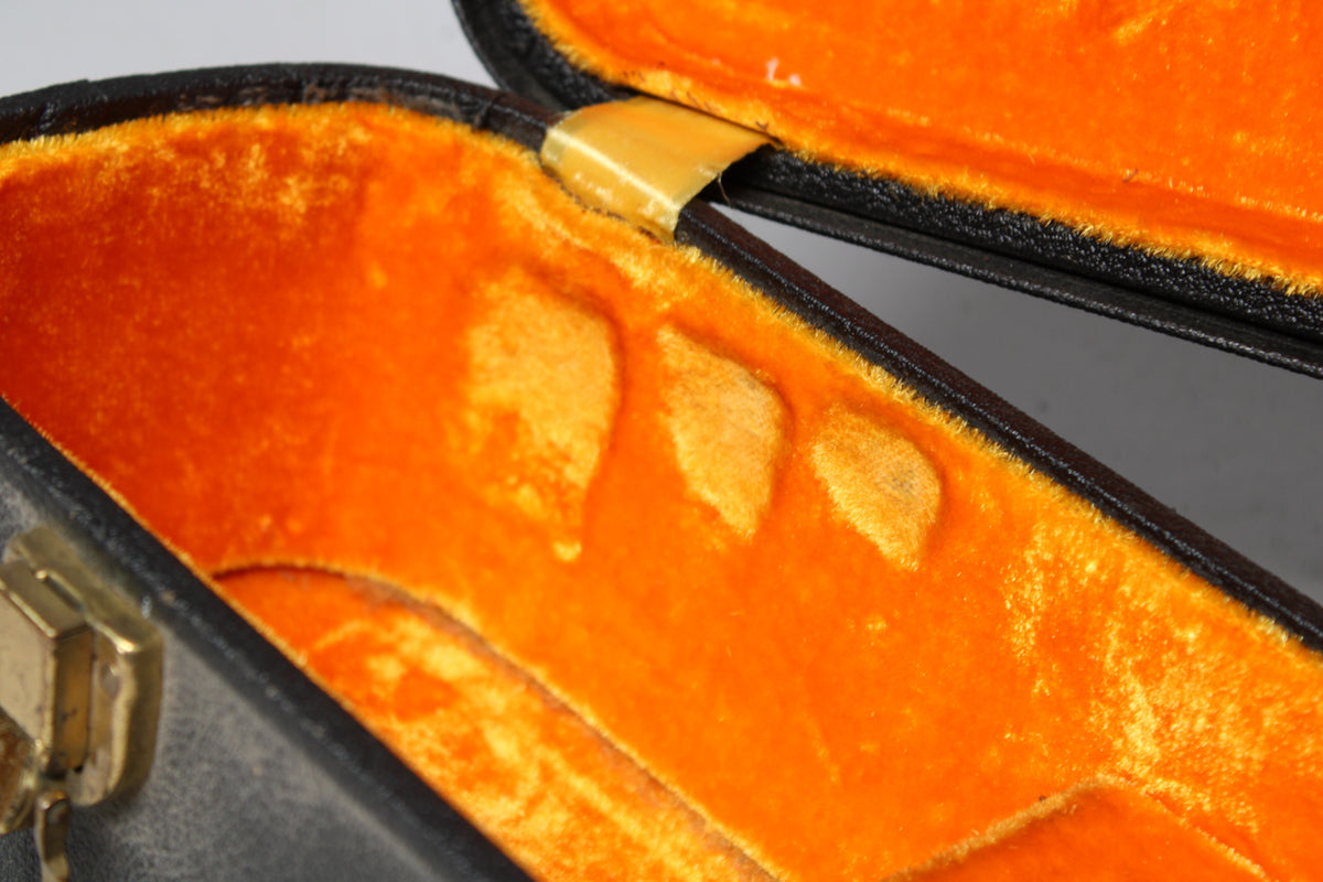 Close-up of the open black case, revealing its bright orange plush interior with three raised pads and a gold-colored hinge.
