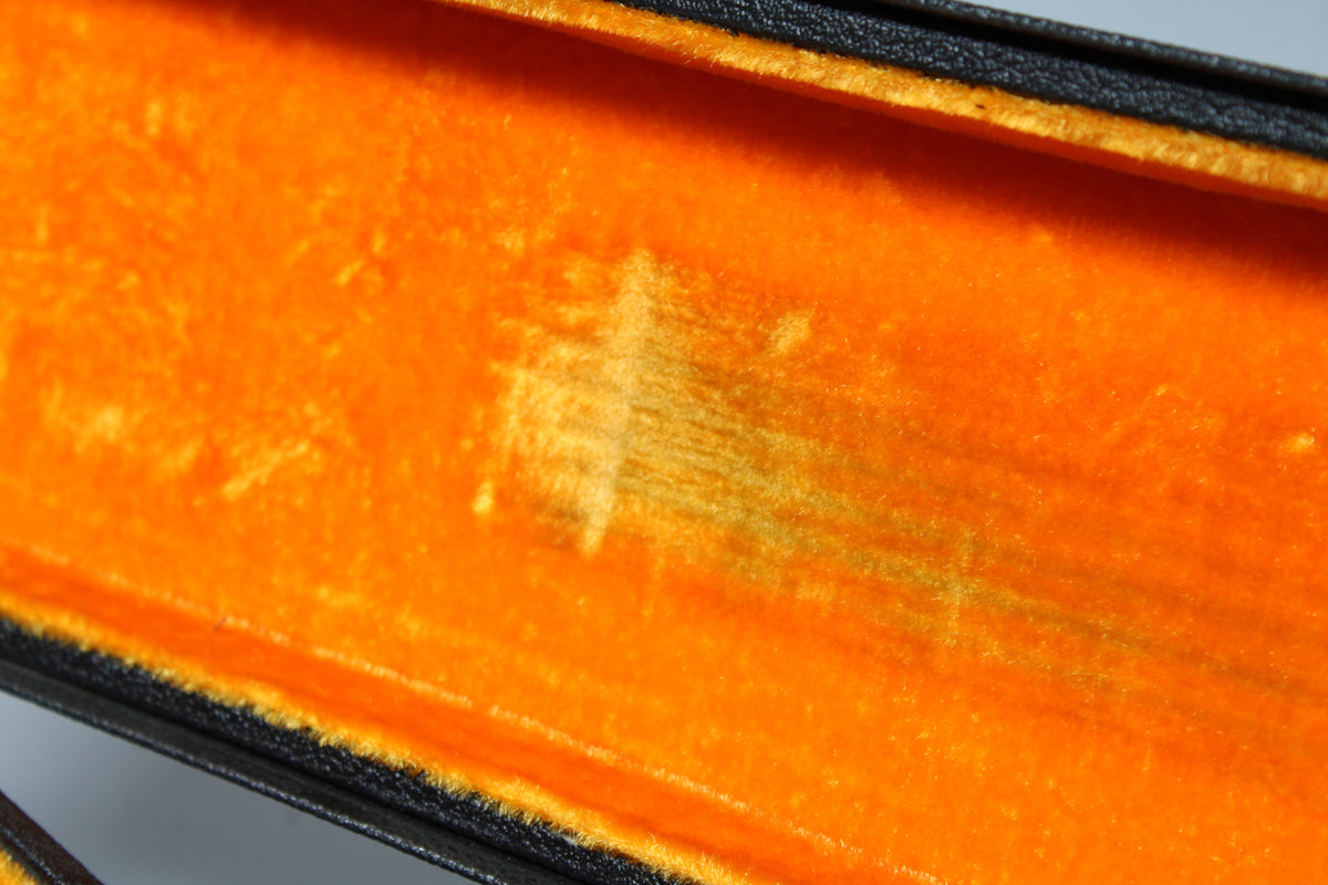 Close-up of the case's bright orange plush lining, showing a large worn patch in the center and some discoloration along the bottom edge.