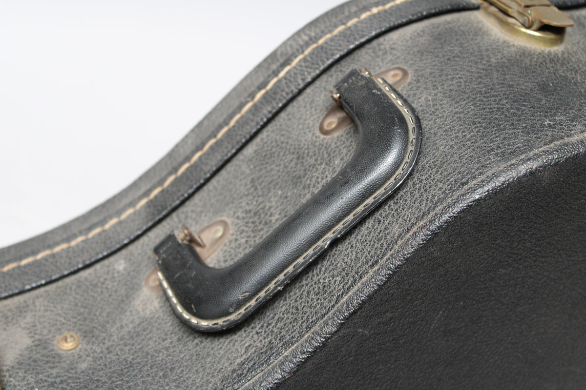 Close-up of the black leather handle on the worn, textured black case, with visible white stitching and brass hardware.