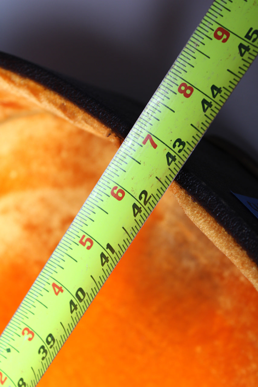 A bright yellow tape measure extends diagonally across the black case, showing the orange plush interior.
