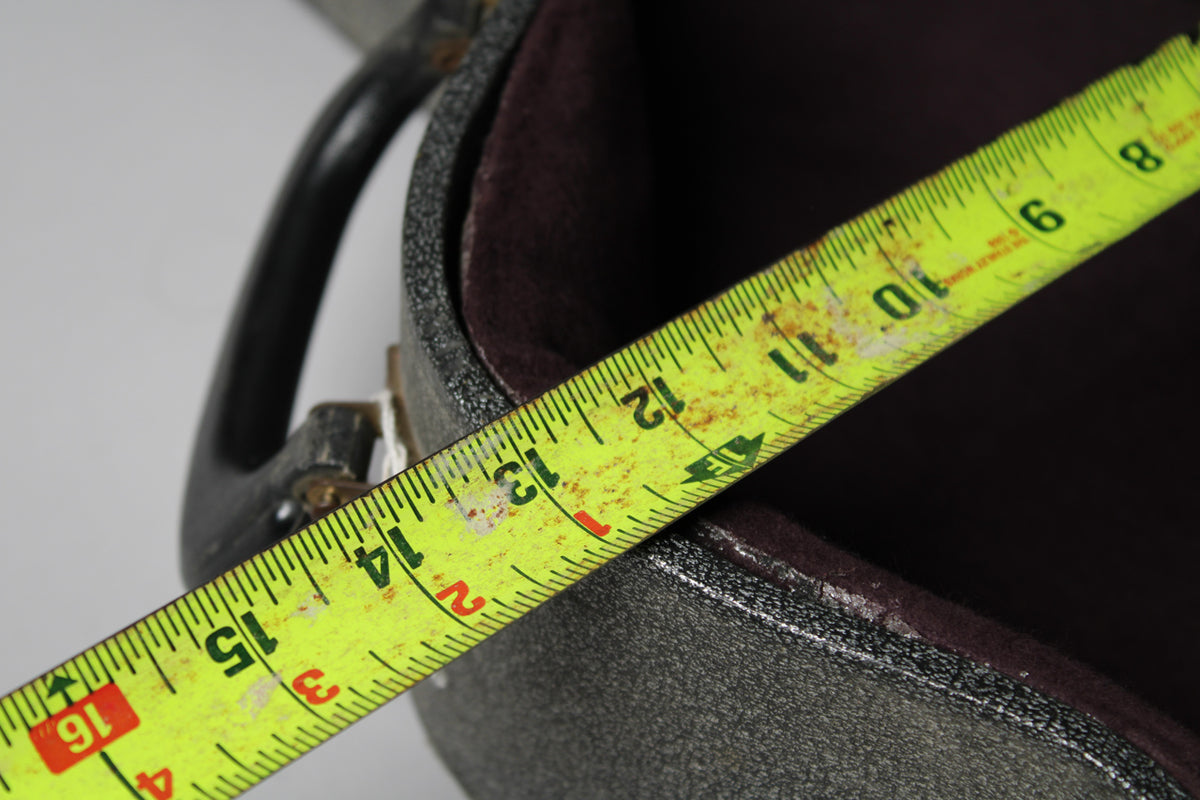 A yellow measuring tape with rust spots extends diagonally across the open, dark gray case, showing the interior lining.