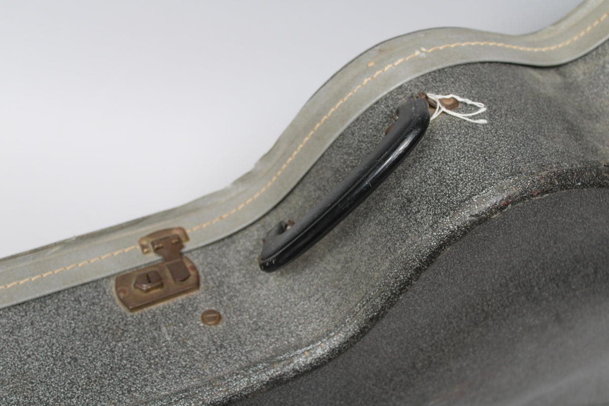 Close-up of the silver sparkle case, showing the black handle, a brass latch, and light wear on the textured exterior.