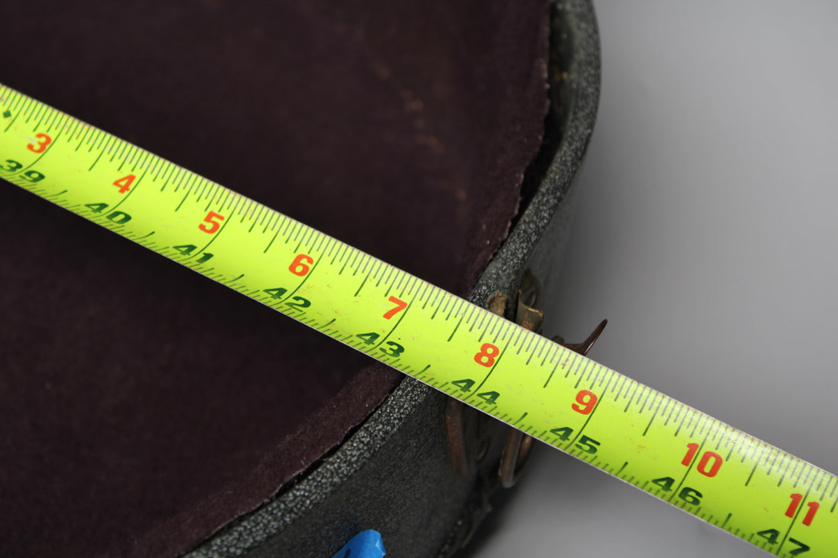A bright yellow measuring tape stretches across the open, dark gray sparkle case, showing its dark red plush interior.