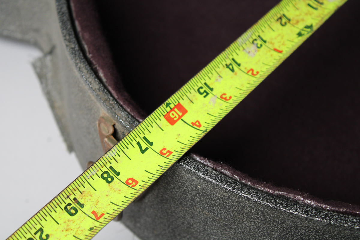 A yellow tape measure spans the dark gray case, showing the interior's dark purple lining and a rusty latch.