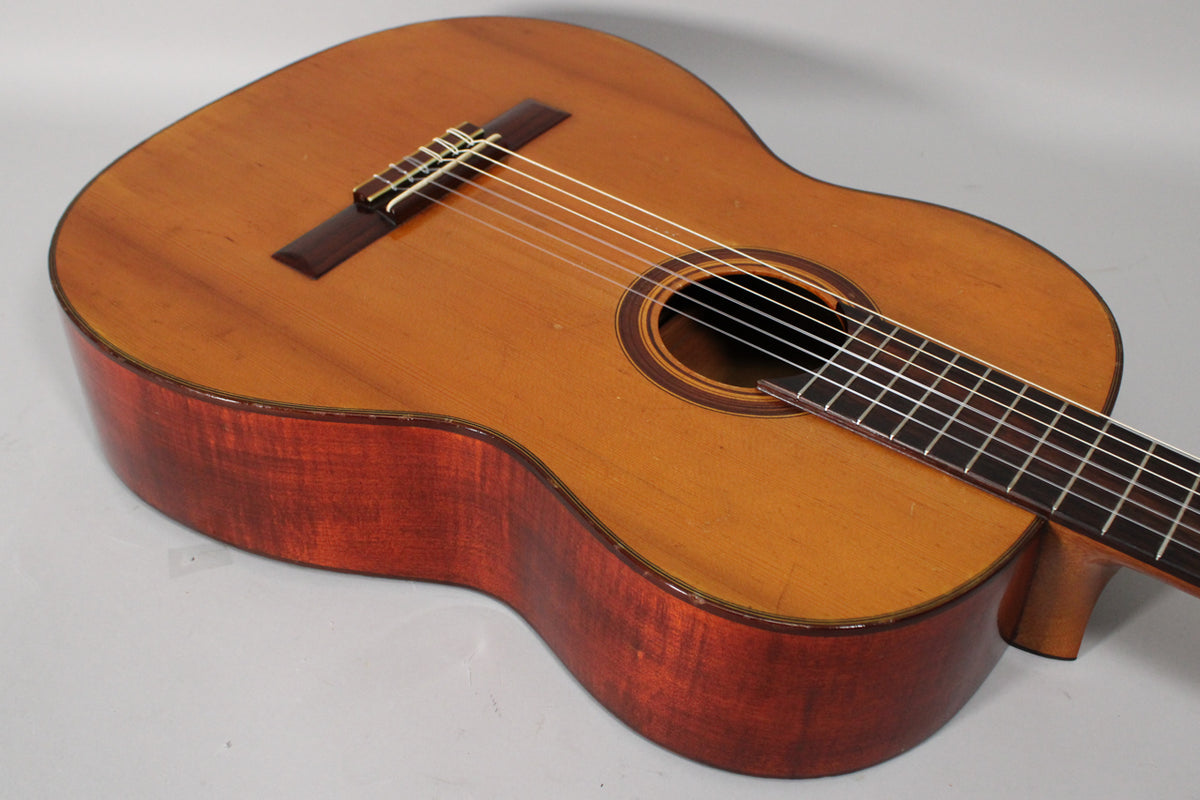 The classical guitar's light brown top and reddish-brown sides are visible from a high angle, showing some finish wear on the edges.