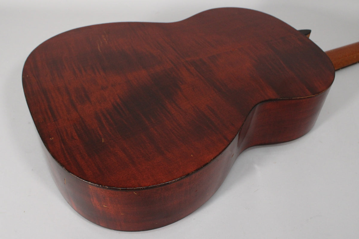 The guitar's dark reddish-brown back and sides are angled from the upper right, showing light wear and wood grain.