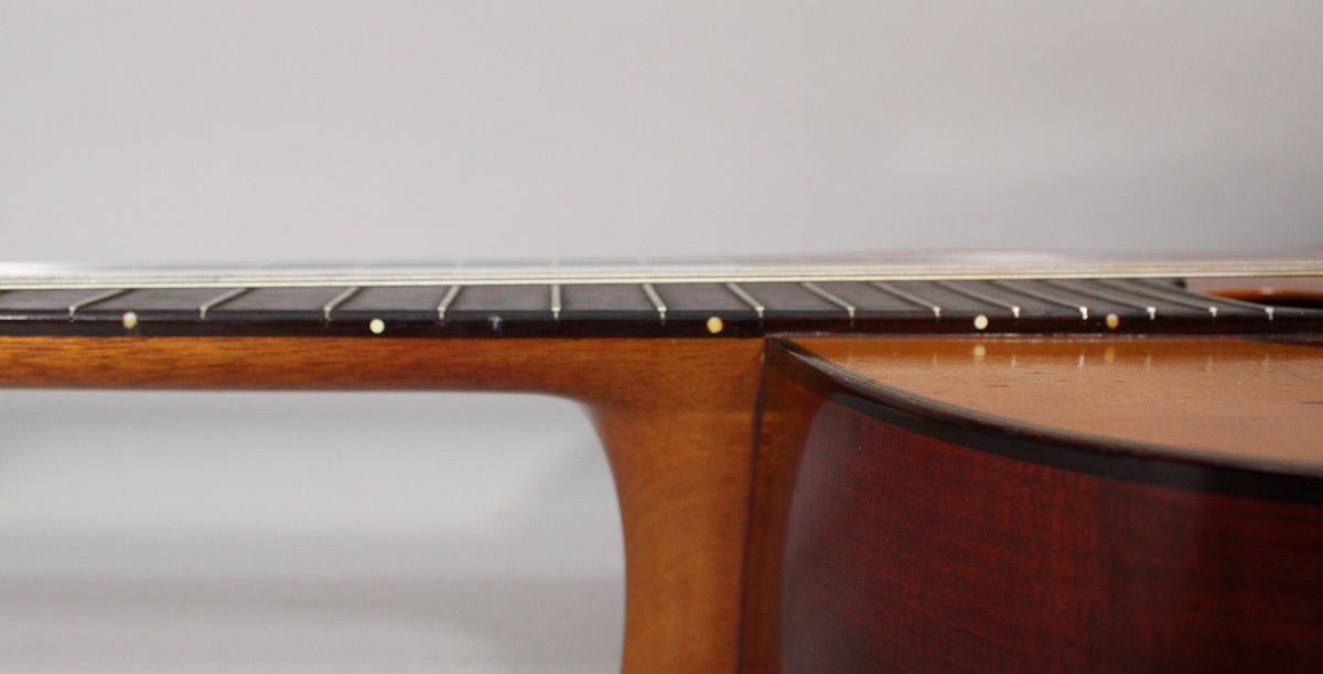 The classical guitar's dark brown fretboard and light brown neck meet the body, with light-colored side dots visible.