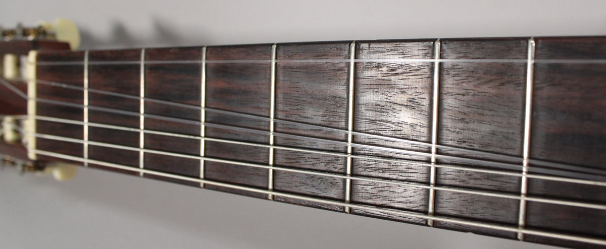 Close-up of the dark brown fretboard and silver frets, with light wear visible on the wood and strings.
