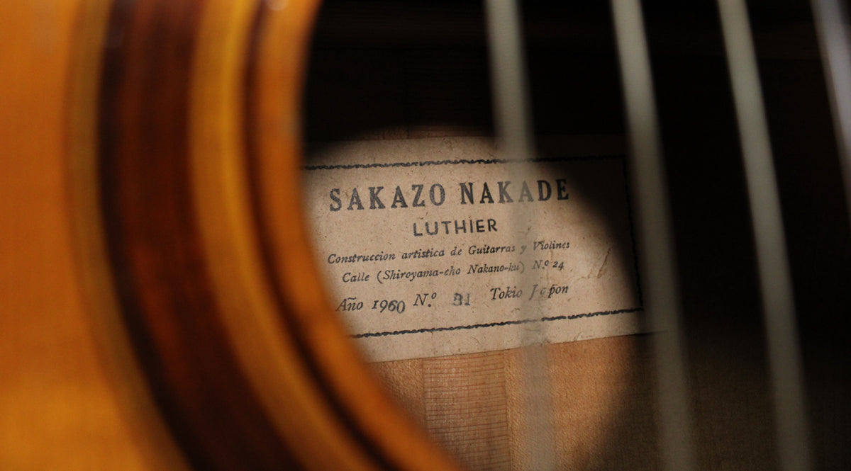 A close-up view through the soundhole of a classical guitar, showing a light-colored, aged paper label with dark text.
