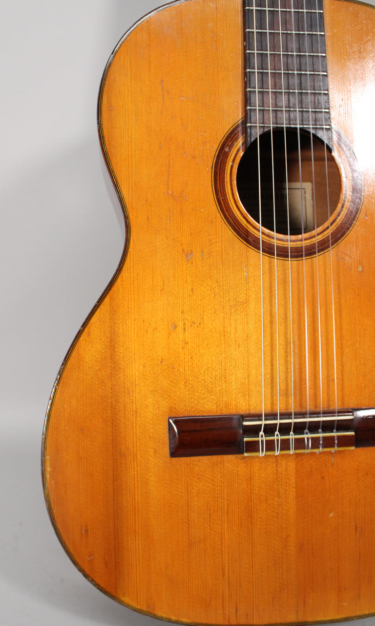 Close-up of the guitar's worn, light brown body, showing the soundhole, dark fretboard, bridge, and visible scratches and finish checking.