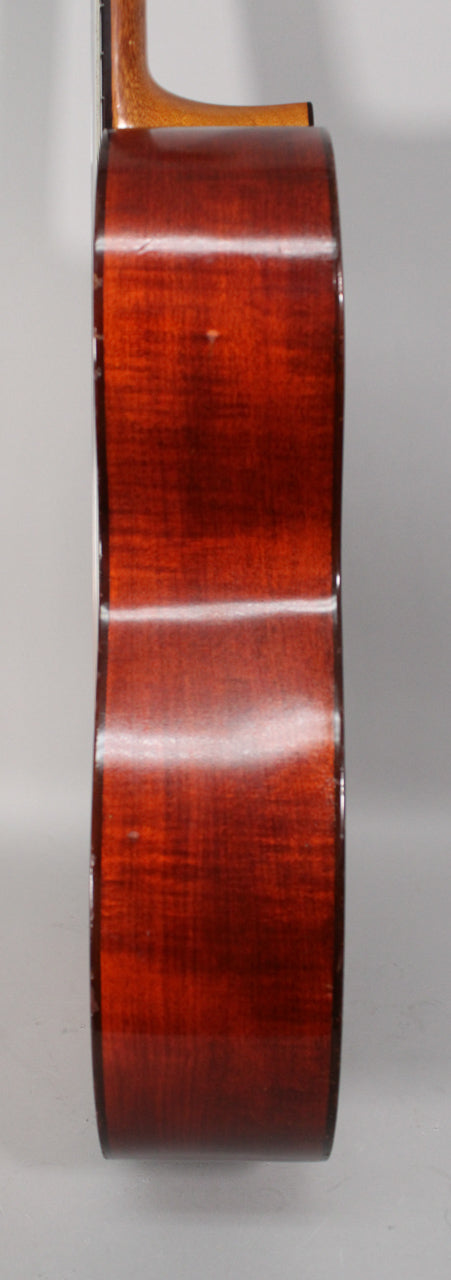 The classical guitar's dark reddish-brown body is shown from the side, revealing some minor nicks and finish wear along the edges.