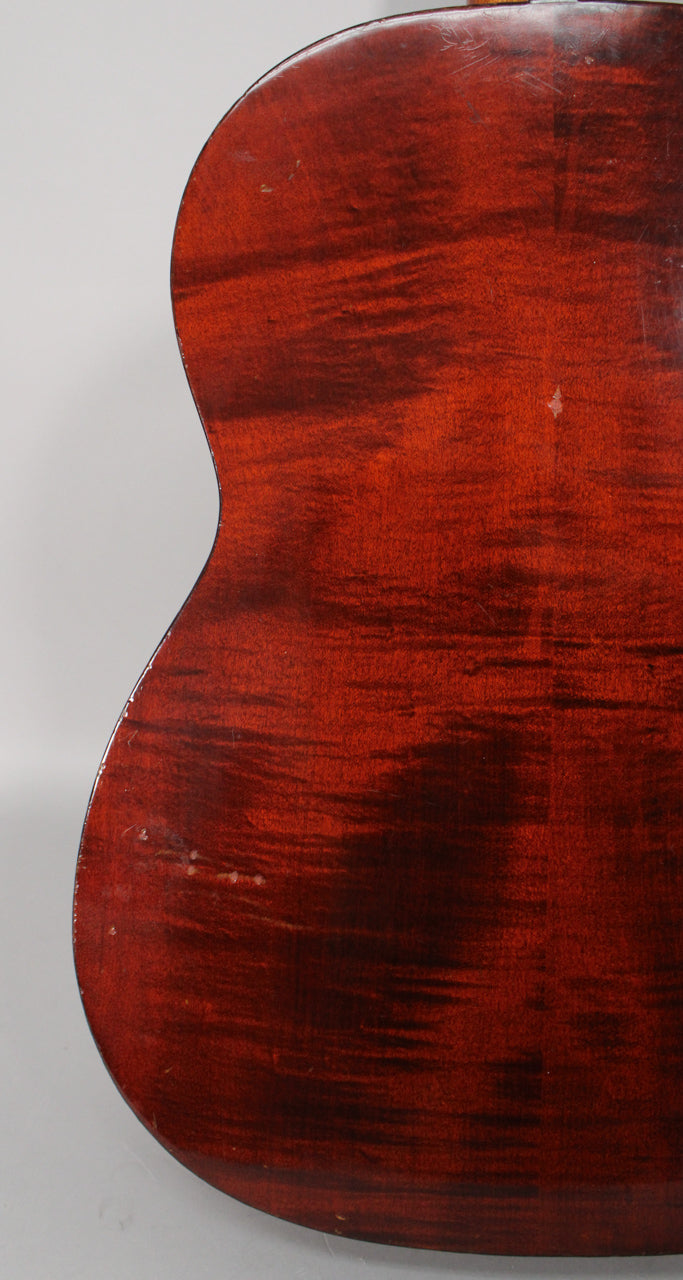 The guitar's dark reddish-brown back shows visible finish wear, scratches, and small dings, especially along the left edge.