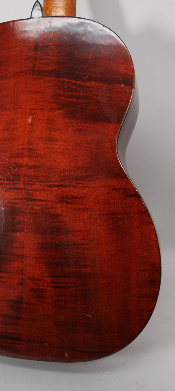 The guitar's dark reddish-brown back, with visible wood grain and minor scratches, is angled to show the upper bout and neck heel.