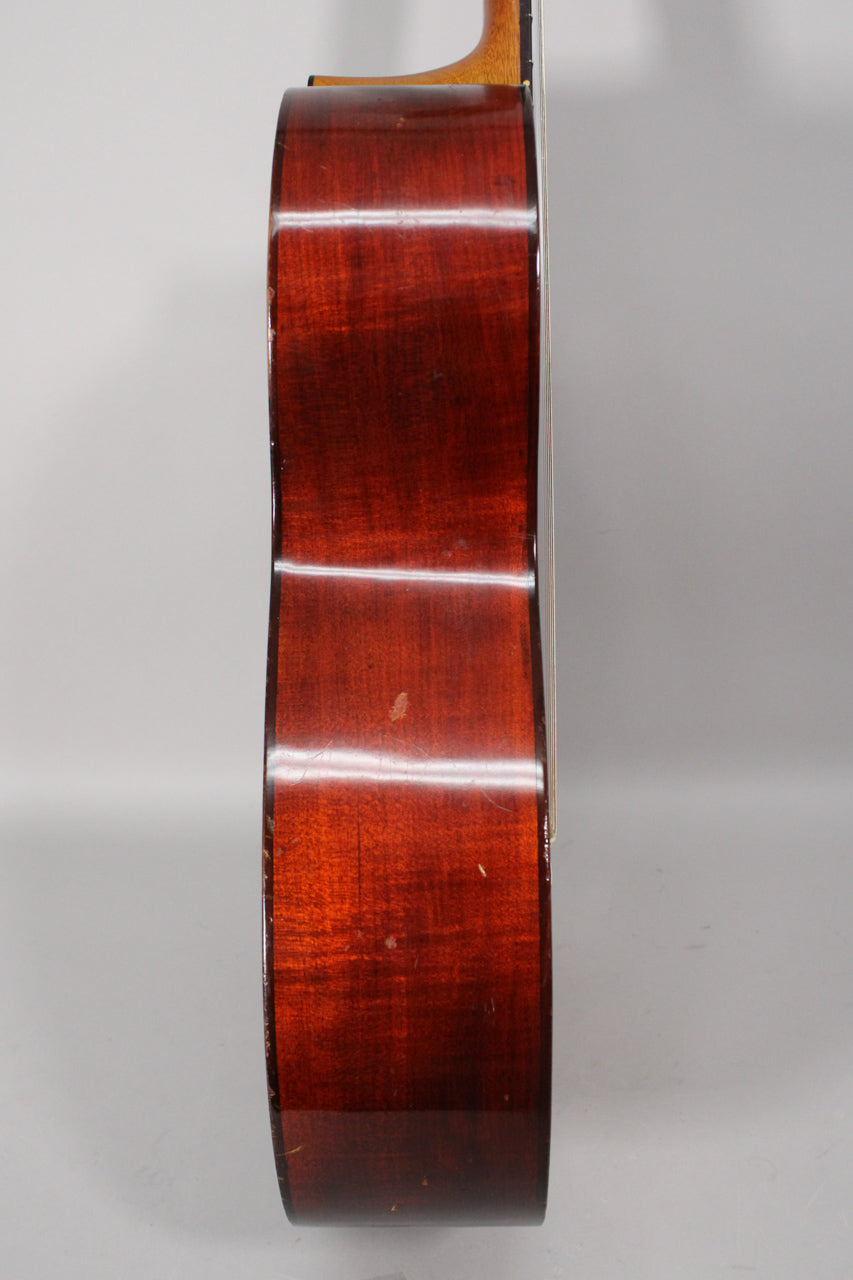 The guitar's dark reddish-brown body is shown from the side, revealing a glossy finish with light scratches and scuffs.