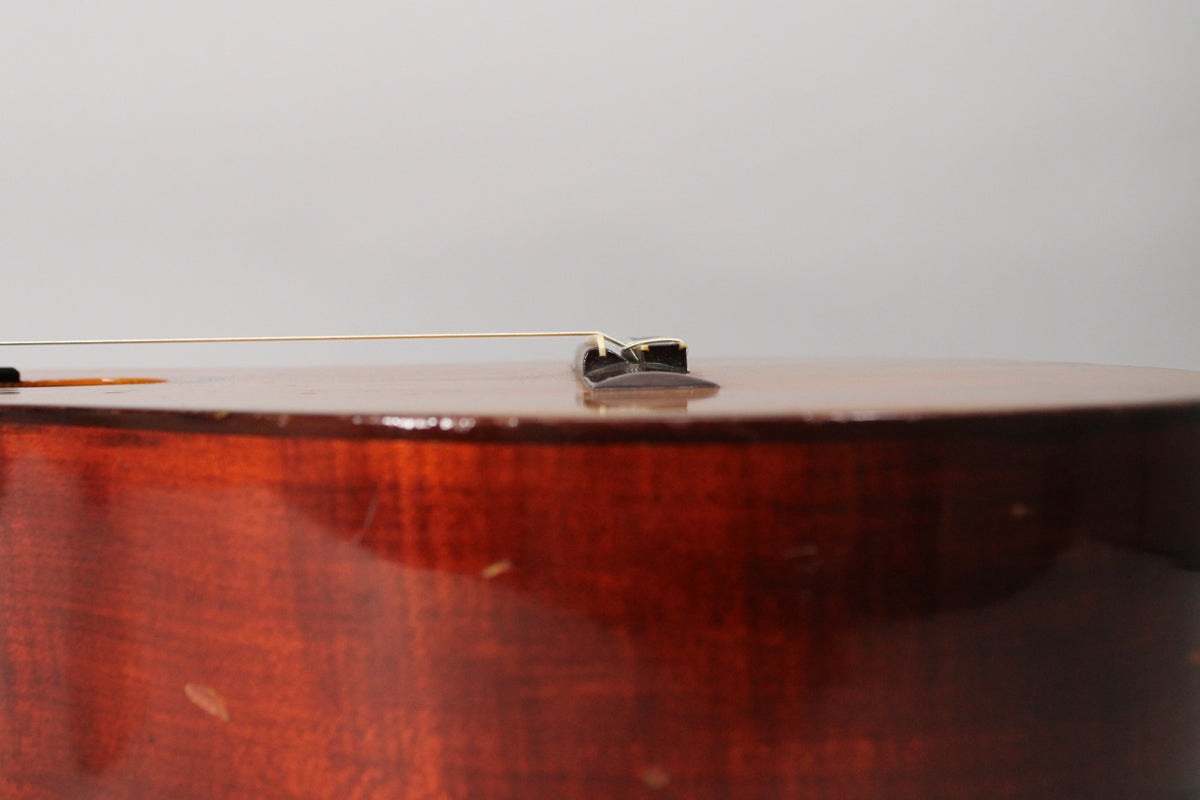 Close-up of the classical guitar's dark brown body and bridge, showing wear and light scratches on the glossy finish.