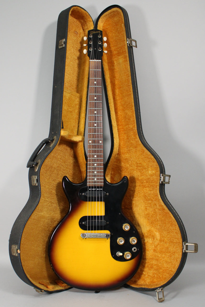 Full-length view of a sunburst electric guitar with a black pickguard, two pickups, and four gold-capped control knobs, resting in its open, plush-lined case.