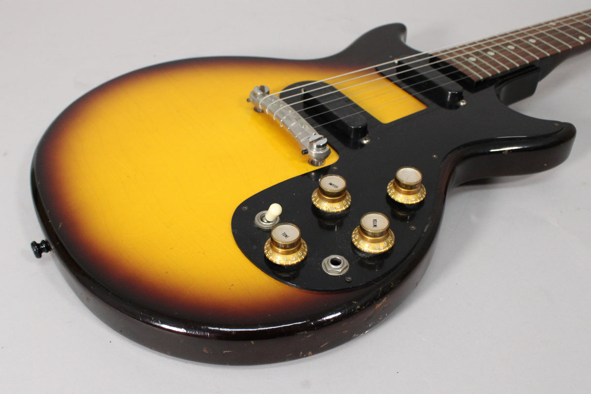 Close-up of the sunburst body, showing the black pickguard, two pickups, four gold-capped knobs, a toggle switch, and finish wear.