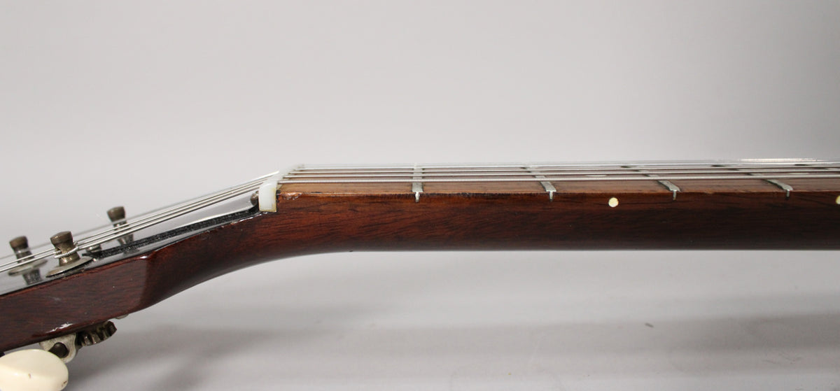 The guitar's dark brown neck and fretboard are viewed from the side, showing the nut, frets, and dot inlays, with some finish wear near the nut.