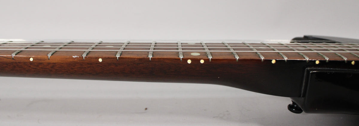 Close-up of the dark brown fretboard with small white dot inlays, showing some wear and a chip near the 7th fret.