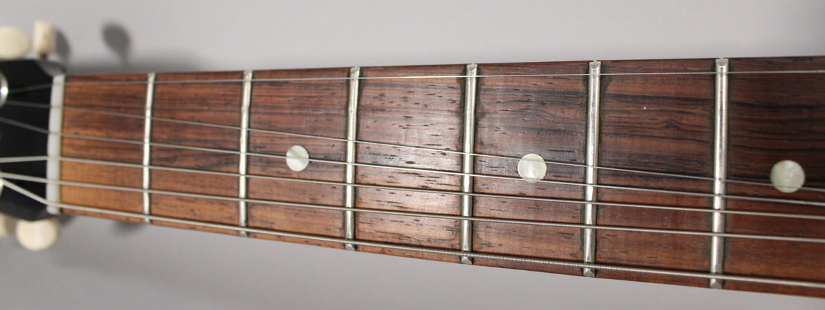 Close-up of the dark rosewood fretboard with six strings, silver frets, and three white dot inlays, showing light wear.