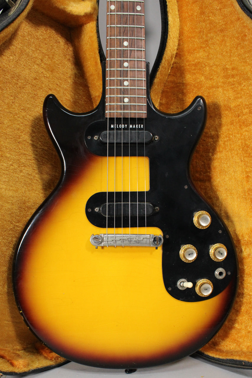 The sunburst guitar's body and lower neck are framed, showing two black single-coil pickups, a chrome bridge, and four gold control knobs.