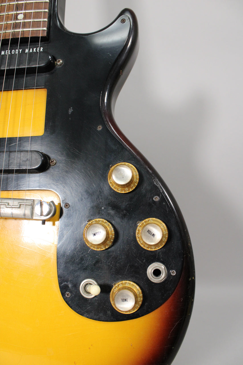 Close-up of the sunburst body, showing the black pickguard with four gold-capped knobs, a white toggle switch, and input jack.
