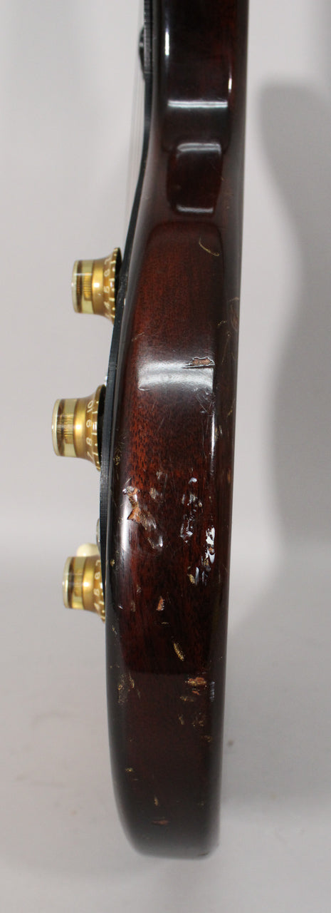 The guitar's dark sunburst body edge, viewed from the side, shows significant finish wear, chips, and checking, with three gold control knobs.